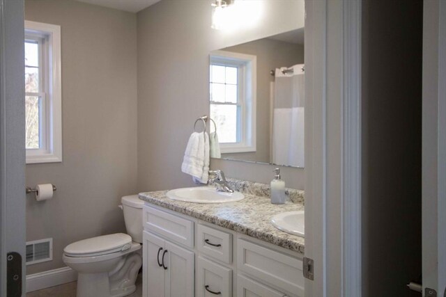 full bathroom with toilet, a sink, visible vents, baseboards, and double vanity