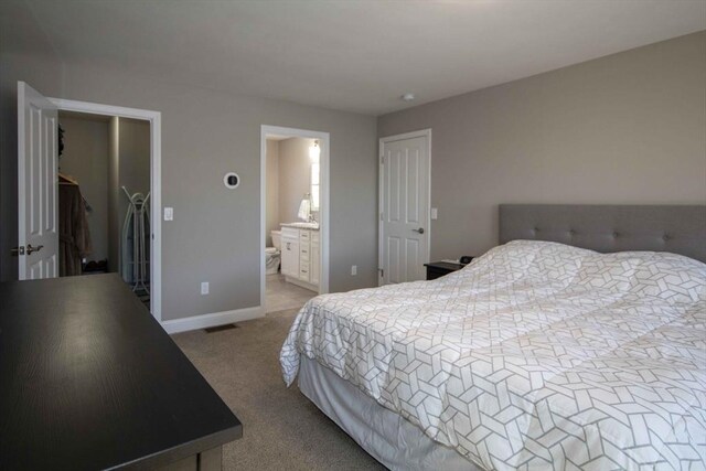 carpeted bedroom featuring visible vents, baseboards, ensuite bath, a walk in closet, and a closet