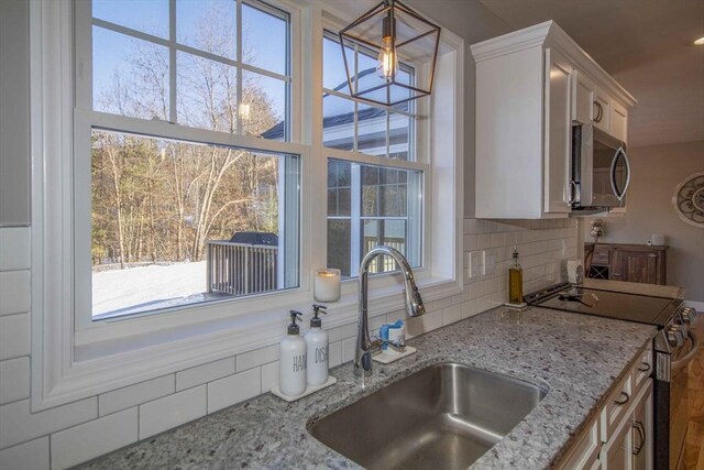 kitchen with light stone counters, a sink, white cabinetry, appliances with stainless steel finishes, and backsplash