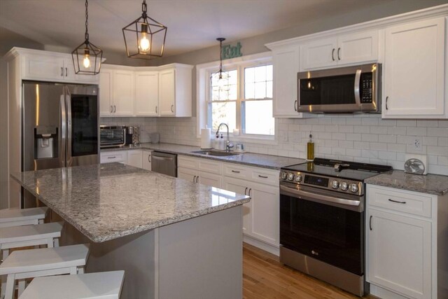 kitchen featuring stainless steel appliances, a sink, light wood-style floors, white cabinets, and decorative backsplash