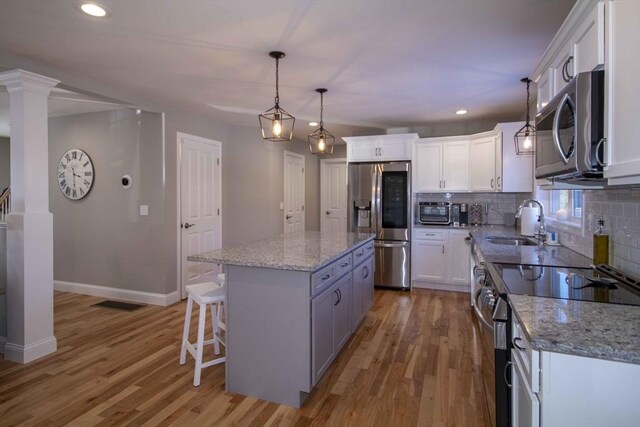 kitchen with tasteful backsplash, appliances with stainless steel finishes, light wood-type flooring, white cabinetry, and a sink