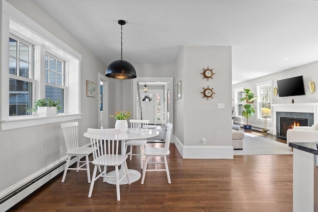 dining room featuring baseboards, a baseboard radiator, a fireplace with flush hearth, and wood finished floors
