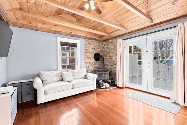 living area featuring lofted ceiling with beams, wooden ceiling, french doors, hardwood / wood-style floors, and a wood stove