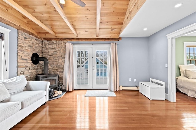 living area featuring lofted ceiling with beams, a baseboard radiator, wood finished floors, a wood stove, and french doors