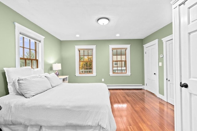 bedroom with baseboards, wood finished floors, a baseboard heating unit, multiple closets, and recessed lighting