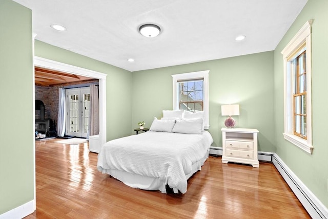 bedroom featuring a wood stove, baseboards, baseboard heating, and wood finished floors