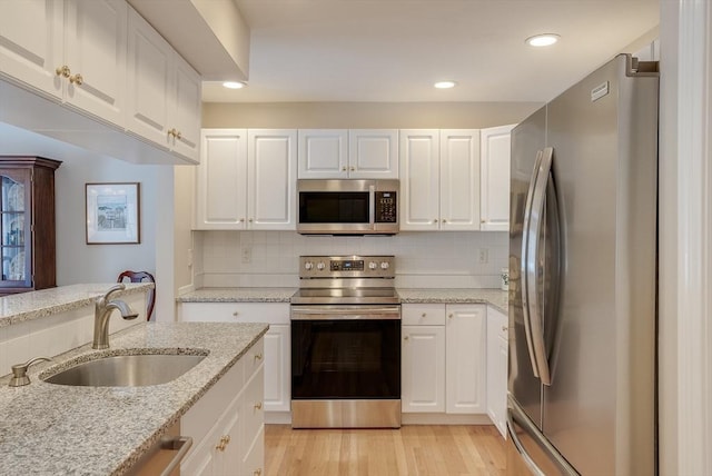 kitchen with sink, light stone counters, stainless steel appliances, decorative backsplash, and white cabinets