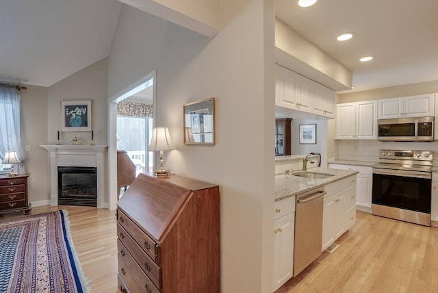 kitchen with sink, light stone counters, light hardwood / wood-style flooring, stainless steel appliances, and white cabinets