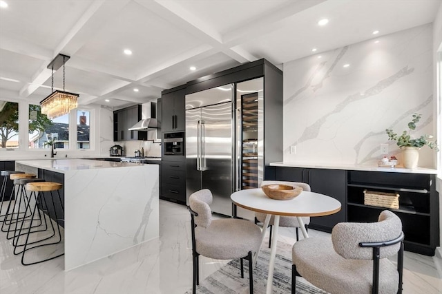 kitchen featuring dark cabinetry, pendant lighting, stainless steel built in fridge, and wall chimney range hood