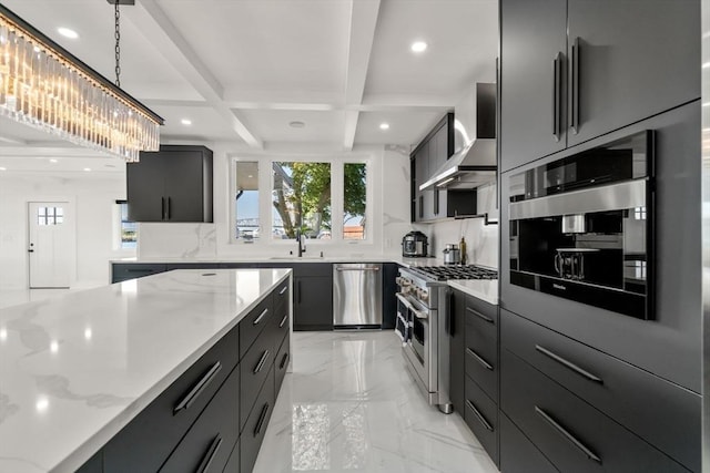 kitchen with appliances with stainless steel finishes, wall chimney range hood, hanging light fixtures, light stone counters, and dark cabinetry