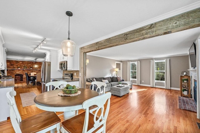 dining area featuring sink, light wood-type flooring, a brick fireplace, rail lighting, and crown molding