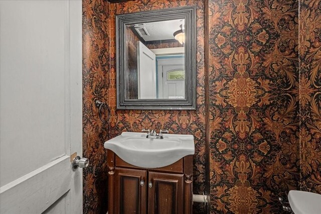 half bath featuring vanity, visible vents, toilet, and wallpapered walls