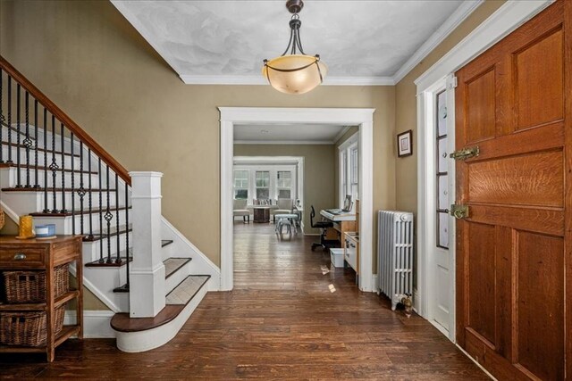 foyer entrance with dark wood-style flooring, ornamental molding, radiator heating unit, and stairway