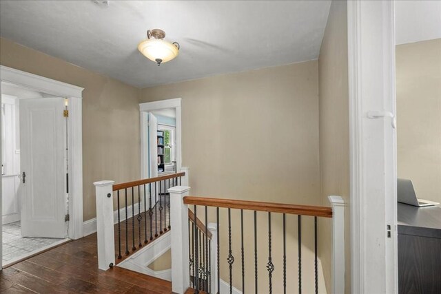 hall featuring baseboards, wood finished floors, and an upstairs landing