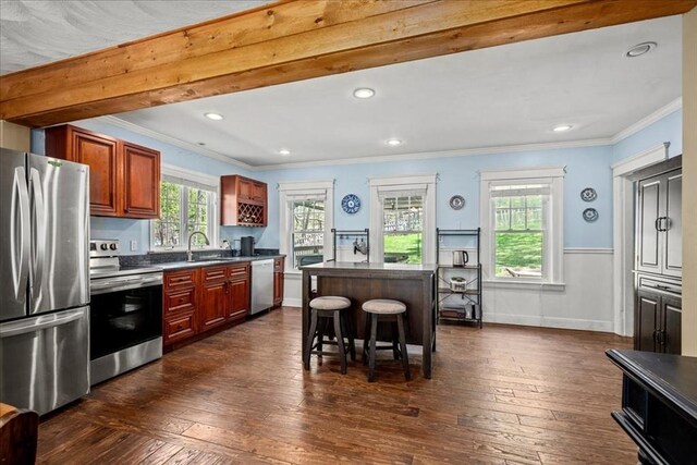 kitchen featuring a breakfast bar area, dark countertops, appliances with stainless steel finishes, ornamental molding, and dark wood-type flooring