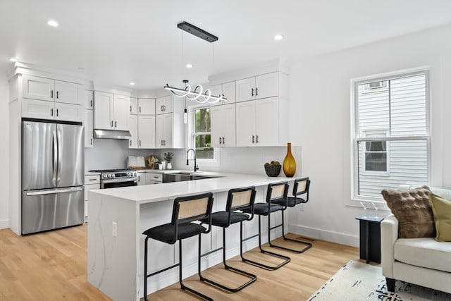 kitchen with light wood-type flooring, stainless steel appliances, decorative light fixtures, and kitchen peninsula