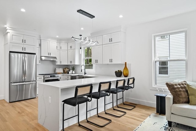 kitchen featuring a peninsula, a breakfast bar area, under cabinet range hood, light wood-style flooring, and appliances with stainless steel finishes