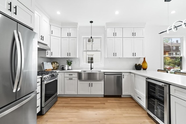 kitchen featuring wine cooler, light countertops, white cabinetry, a sink, and appliances with stainless steel finishes