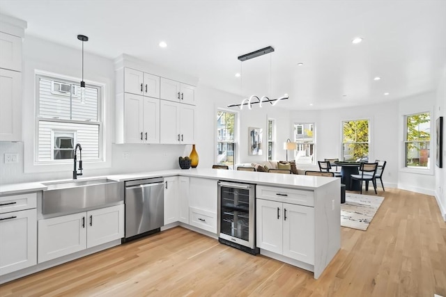 kitchen featuring dishwasher, a sink, a peninsula, wine cooler, and light wood-style flooring