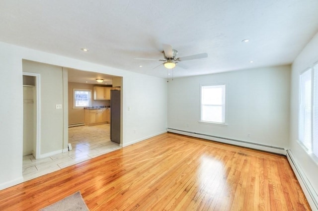 empty room with ceiling fan, light hardwood / wood-style floors, and a baseboard heating unit