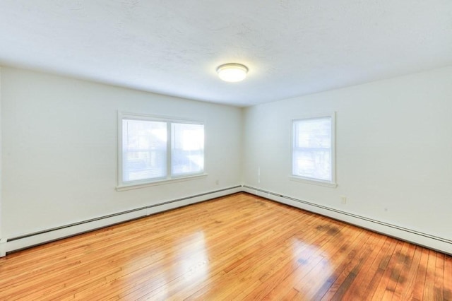 unfurnished room with a baseboard heating unit and light wood-type flooring