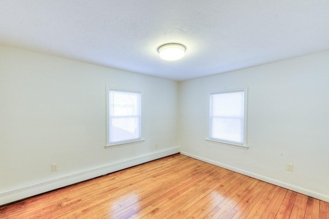 empty room with light hardwood / wood-style flooring, a baseboard heating unit, and a wealth of natural light