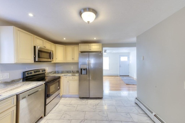 kitchen with stainless steel appliances, light stone counters, baseboard heating, and cream cabinetry