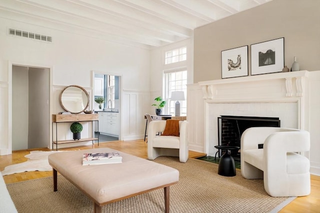 65 Glen Rd Unit H4, Brookline, MA 02445 - living area with light wood-type flooring, beamed ceiling, a fireplace, a towering ceiling, and a decorative wall