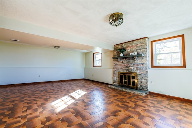 unfurnished living room featuring a healthy amount of sunlight, a stone fireplace, and a textured ceiling