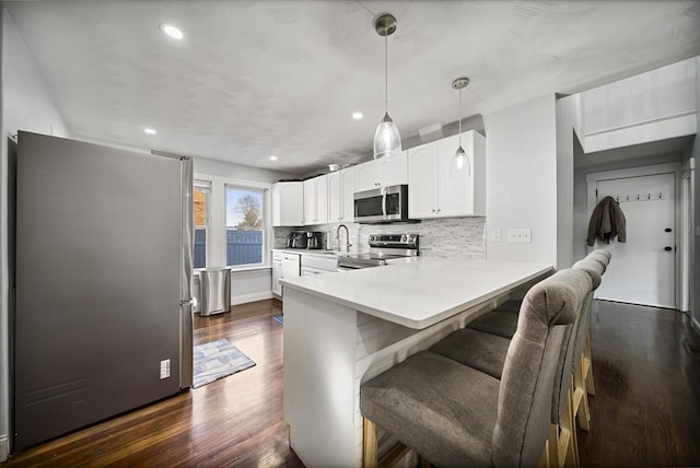 kitchen featuring kitchen peninsula, appliances with stainless steel finishes, a breakfast bar, pendant lighting, and white cabinetry