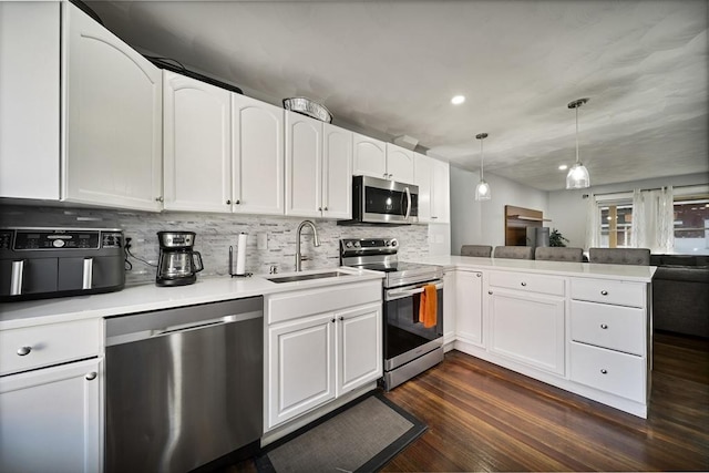 kitchen featuring white cabinetry, sink, kitchen peninsula, decorative light fixtures, and appliances with stainless steel finishes