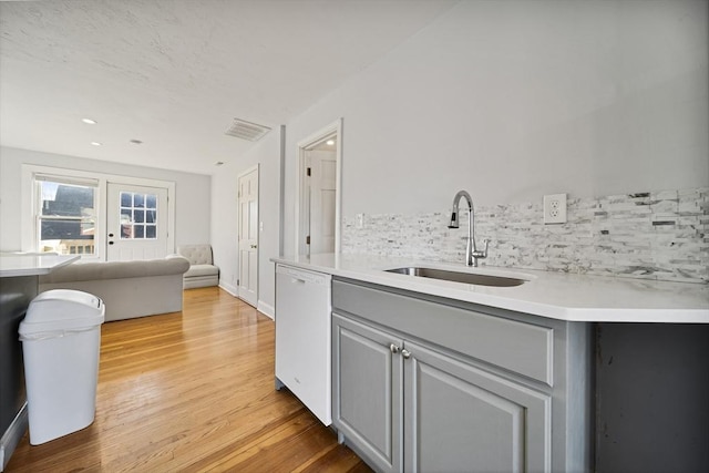 kitchen with sink, light hardwood / wood-style flooring, white dishwasher, gray cabinets, and decorative backsplash