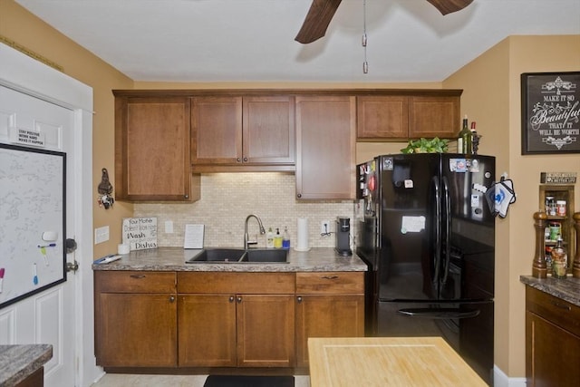 kitchen with decorative backsplash, brown cabinetry, a ceiling fan, a sink, and freestanding refrigerator