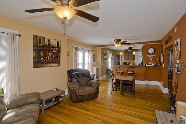 living area with a ceiling fan, baseboards, and light wood-style flooring