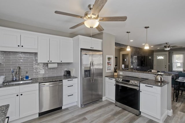 kitchen featuring a ceiling fan, appliances with stainless steel finishes, light wood-type flooring, a sink, and a peninsula