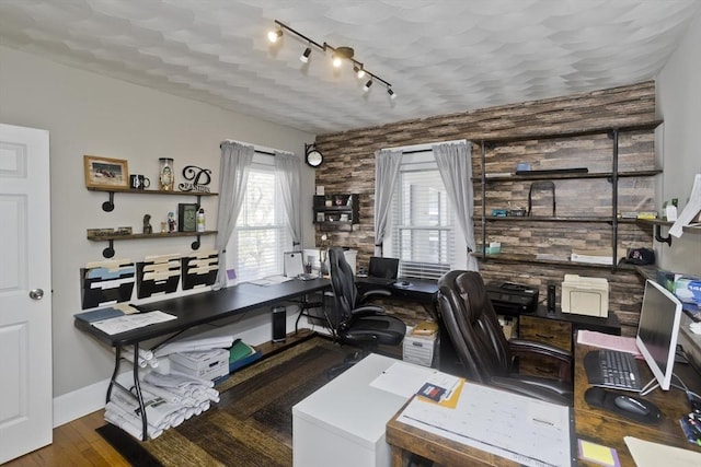 home office featuring wood finished floors, rail lighting, baseboards, and an accent wall