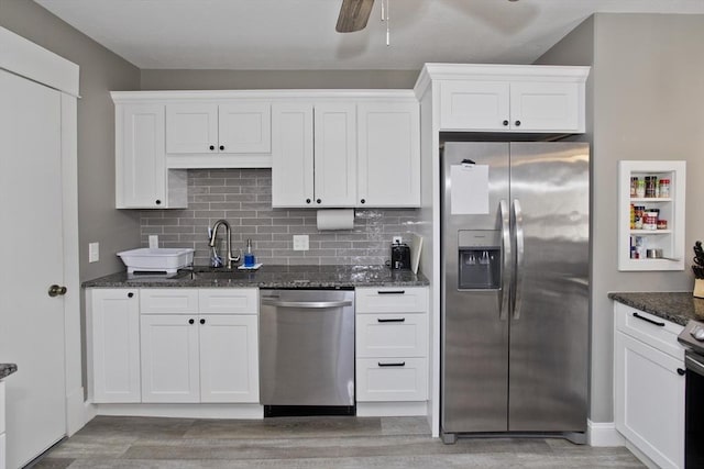 kitchen with light wood-style floors, dark stone counters, stainless steel appliances, white cabinetry, and backsplash