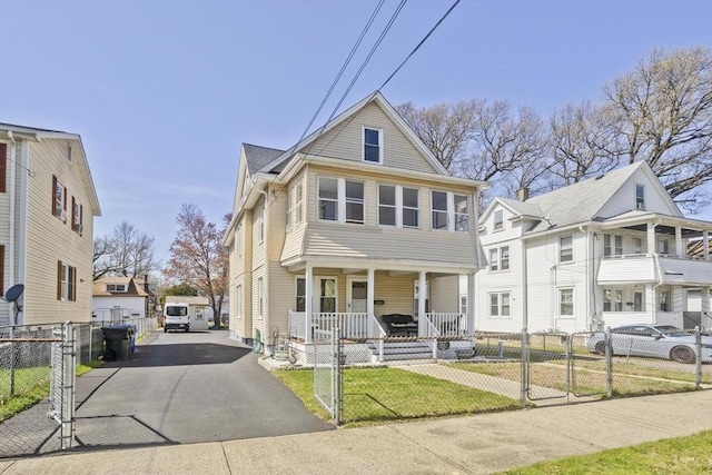 traditional style home with a porch, driveway, a fenced front yard, a gate, and a front lawn