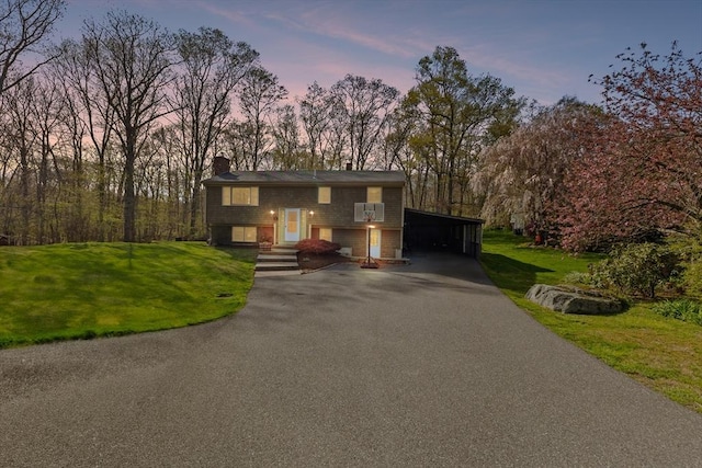 bi-level home with a lawn, a carport, a chimney, and aphalt driveway