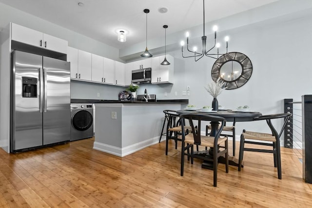 kitchen featuring washer / dryer, dark countertops, appliances with stainless steel finishes, a peninsula, and light wood-type flooring