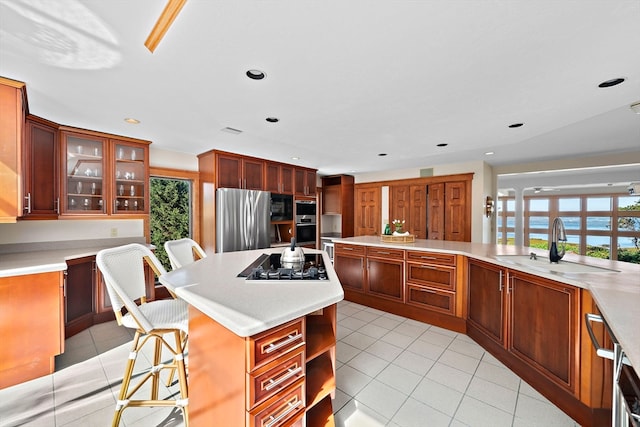 kitchen with light tile patterned flooring, sink, black appliances, a kitchen breakfast bar, and a center island