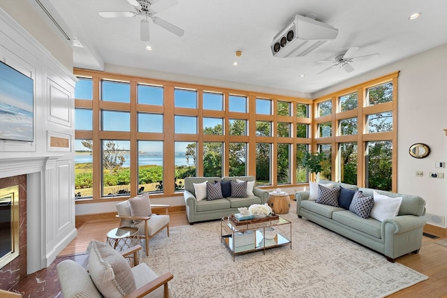 living room with ceiling fan, light hardwood / wood-style flooring, a premium fireplace, and a wealth of natural light