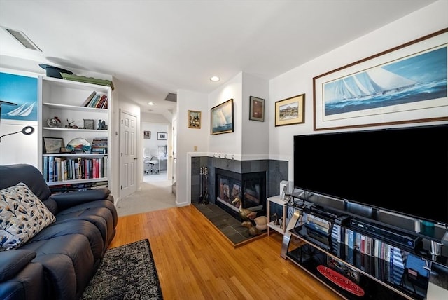 living room featuring a tiled fireplace, visible vents, recessed lighting, and wood finished floors