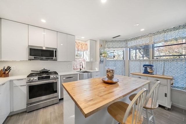 kitchen with a sink, backsplash, white cabinetry, stainless steel appliances, and wooden counters