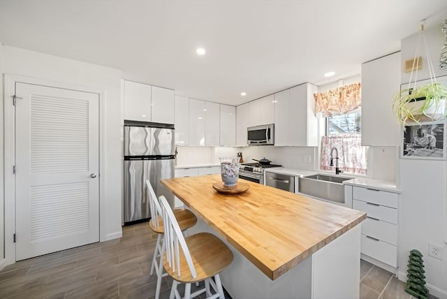 kitchen with a sink, stainless steel appliances, white cabinetry, a kitchen breakfast bar, and modern cabinets