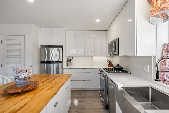 kitchen with modern cabinets, a sink, stainless steel appliances, white cabinets, and wood tiled floor