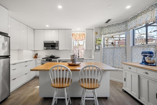 kitchen featuring wood finish floors, a breakfast bar, appliances with stainless steel finishes, white cabinets, and wooden counters