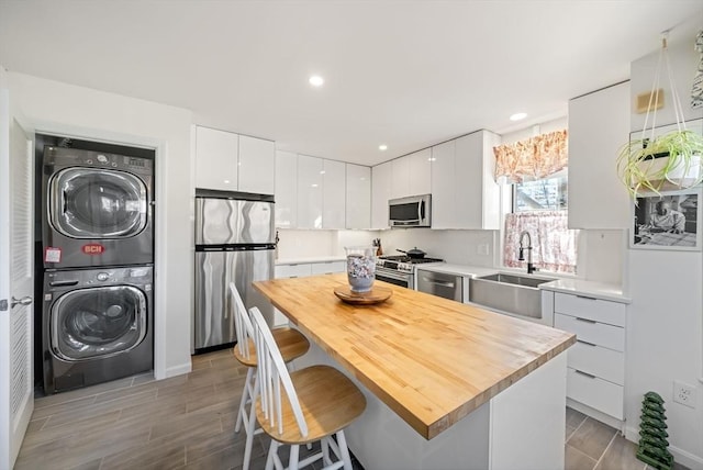 kitchen with stacked washer / dryer, appliances with stainless steel finishes, a kitchen breakfast bar, white cabinets, and a sink