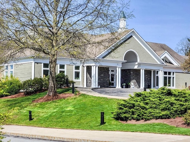 view of front of home with a chimney, stone siding, and a front yard