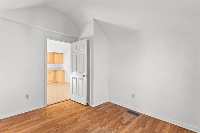 additional living space with visible vents, baseboards, light wood-style flooring, and vaulted ceiling